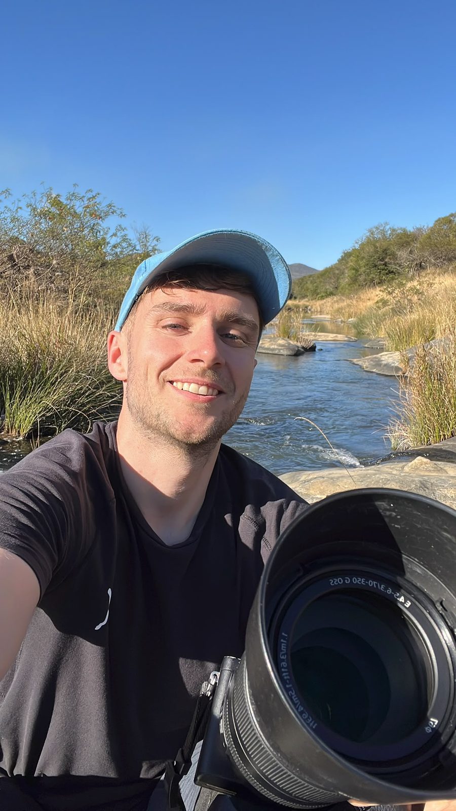 Théophane Piette au bord d’une rivière en Afrique du Sud, téléobjectif en main